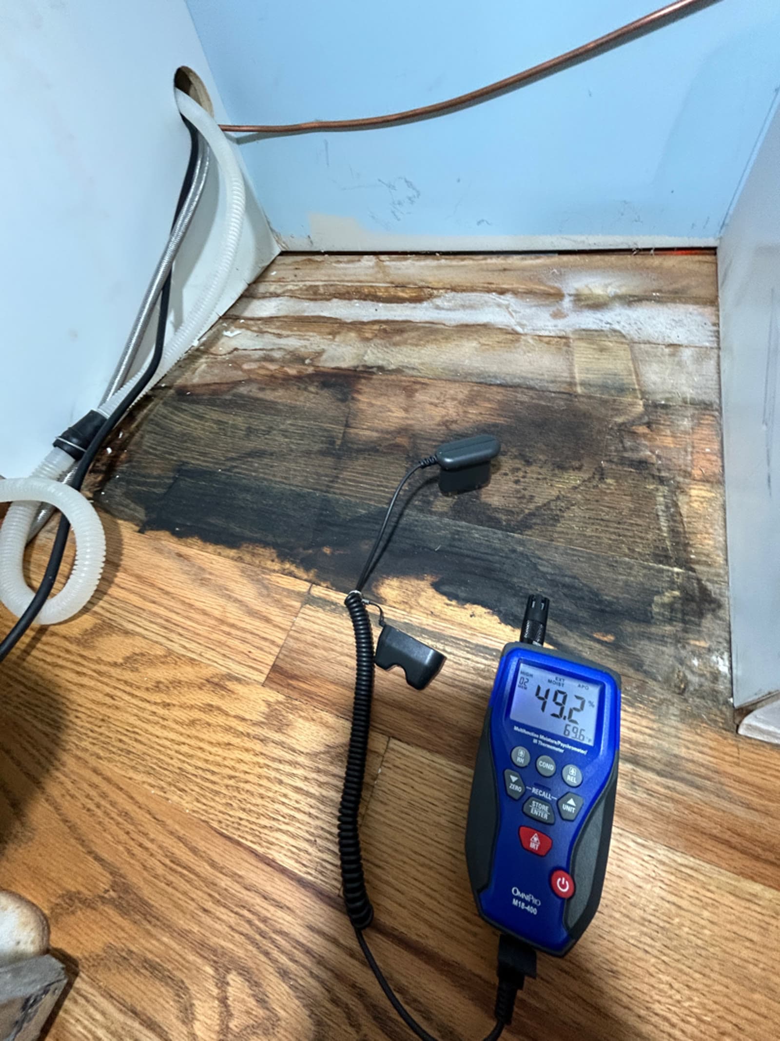 Moisture meter reading beside blackened water damaged hardwood flooring in an East Lyme, CT home