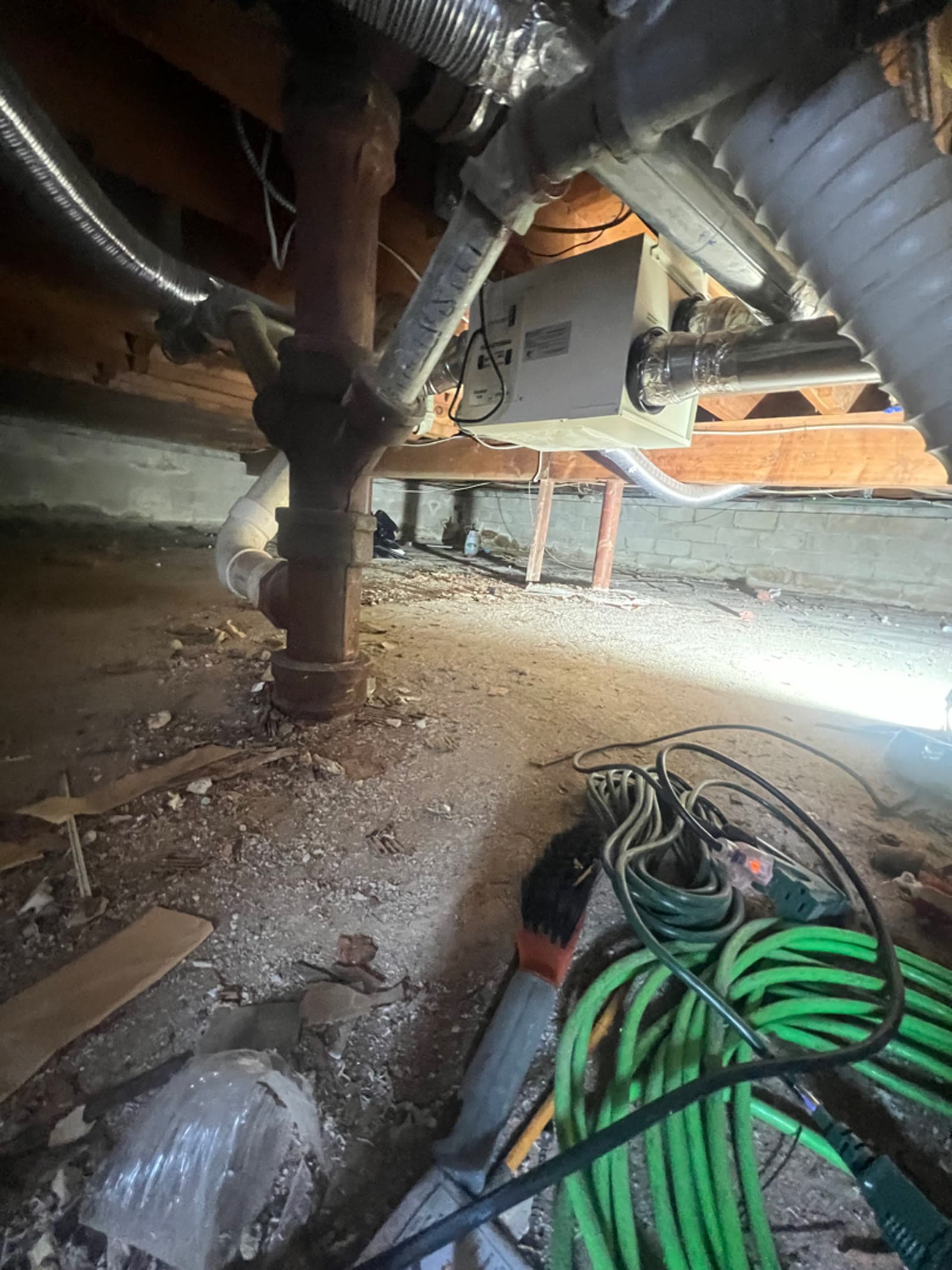 Crawl space under a Hartsdale, NY home with pipework, ductwork and debris across the floor before cleaning