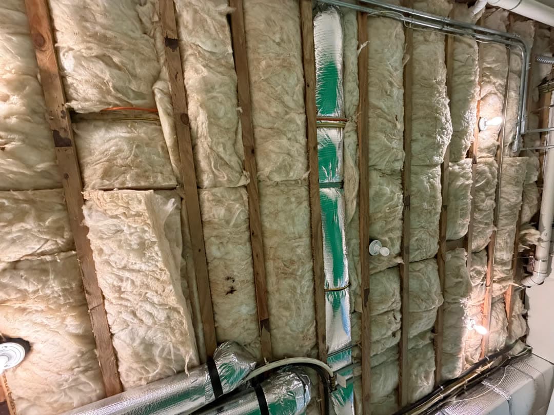 Stained fiberglass batt insulation in the exposed ceiling joists over a basement laundry room in New Canaan, CT