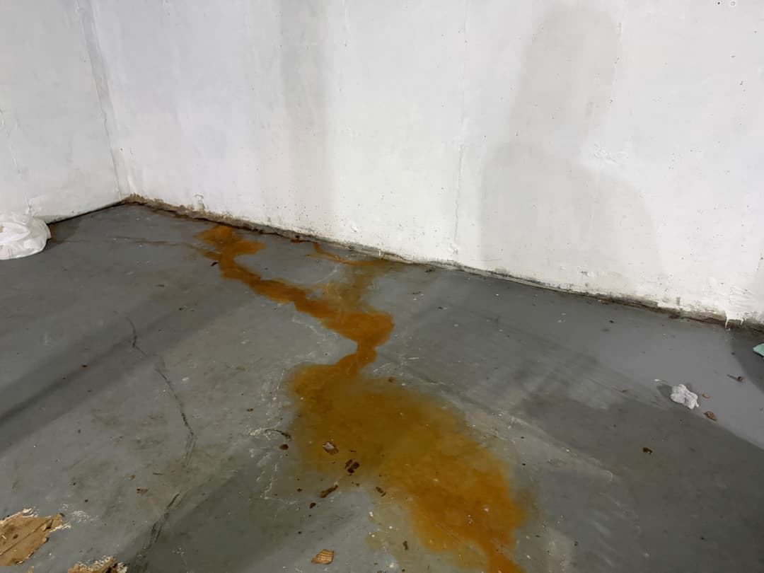 Rust stained water trail running from the foundation wall out across the concrete slab of a Norwich, CT basement