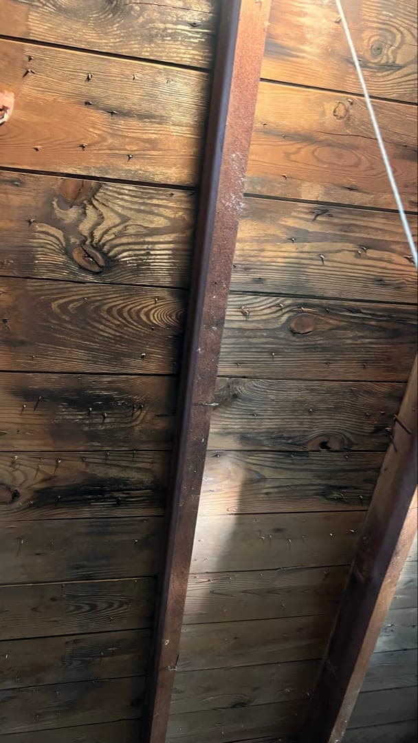 Dark staining across the underside of the plank roof boards in the attic of a pre war West Hartford, CT home before cleaning