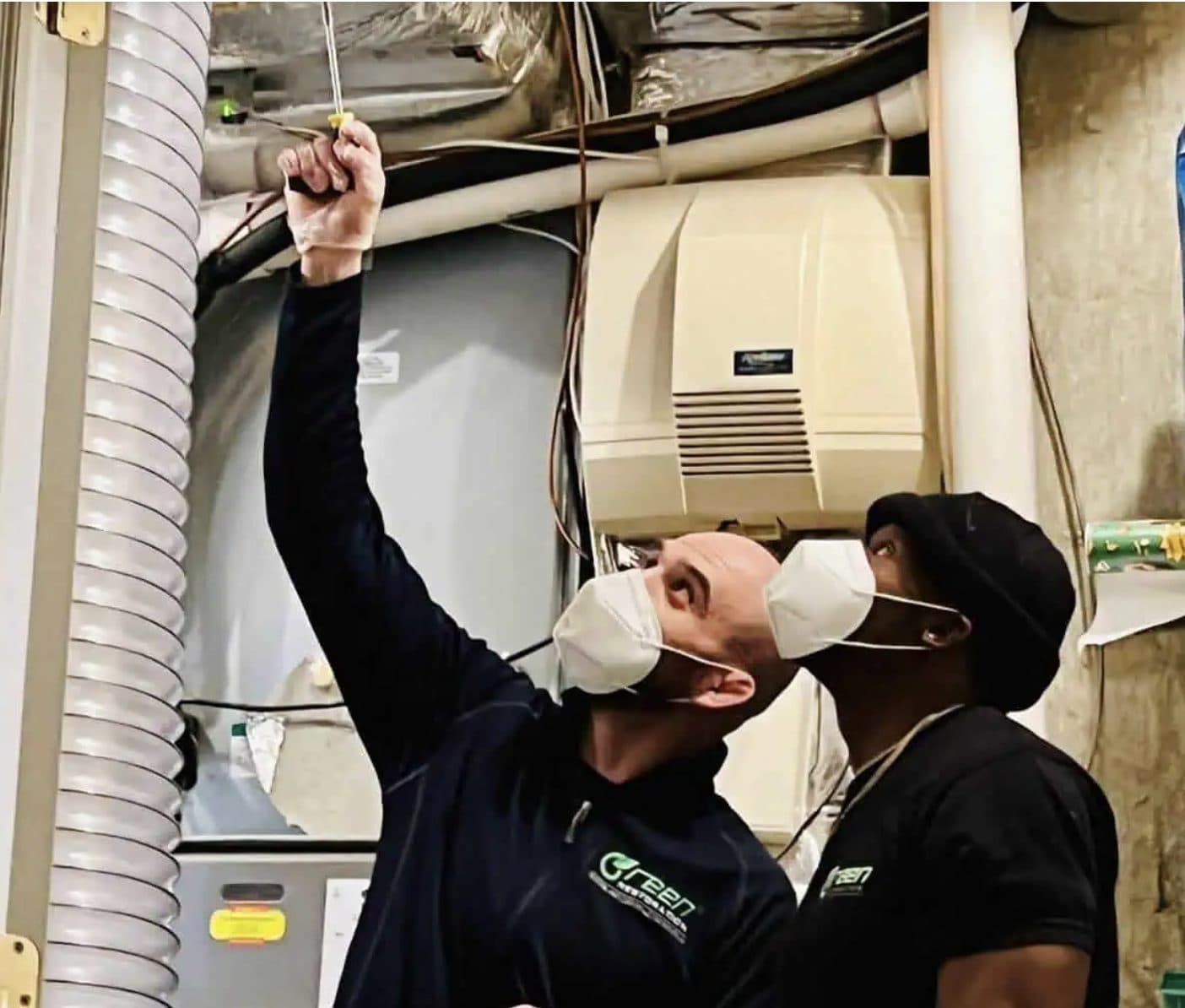 Two Green Restoration technicians in N95 respirators removing register screws at a basement HVAC plenum during NADCA source-removal air duct cleaning in Norwalk CT