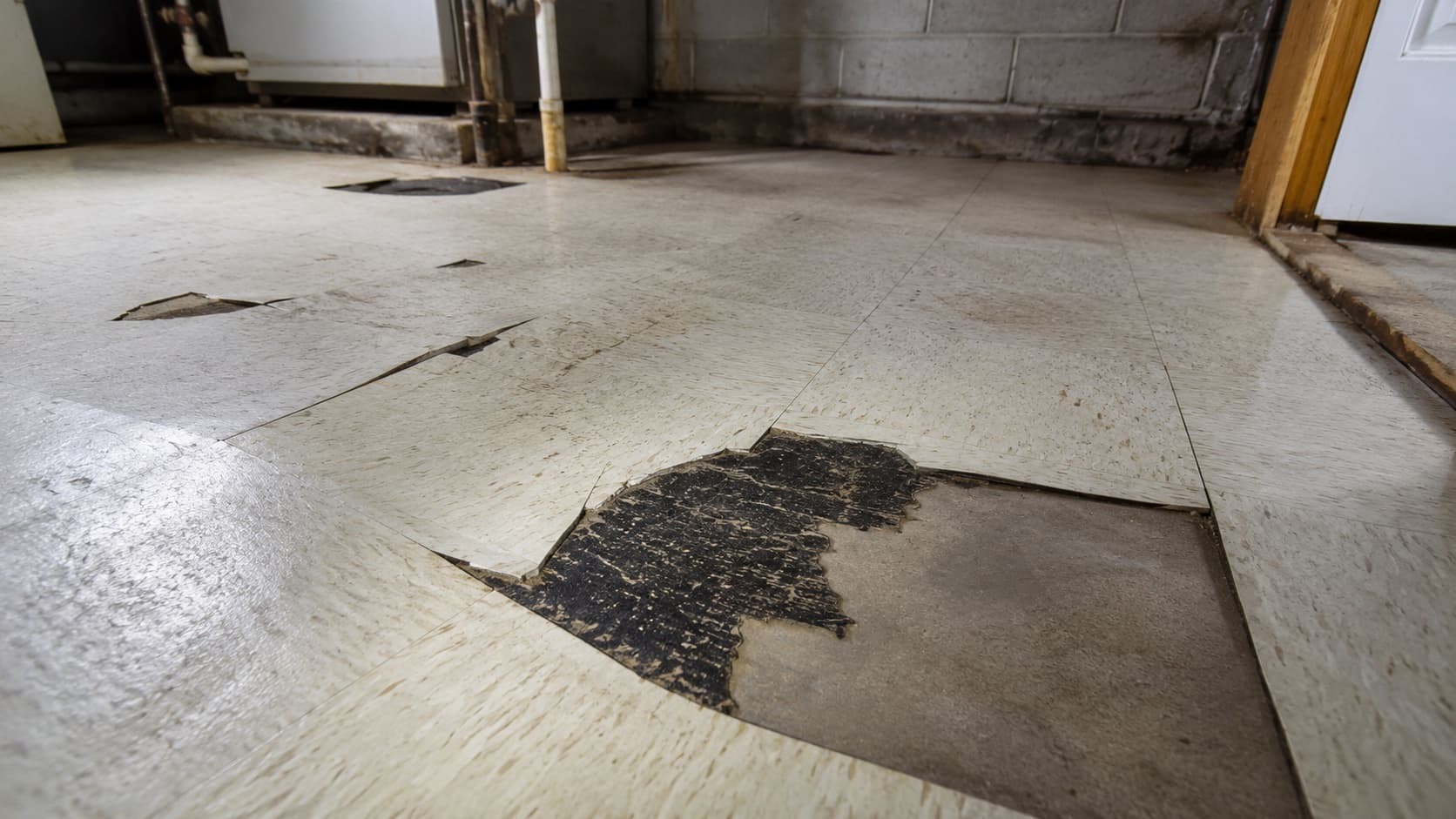 Damaged asbestos floor tile with black mastic adhesive exposed underneath