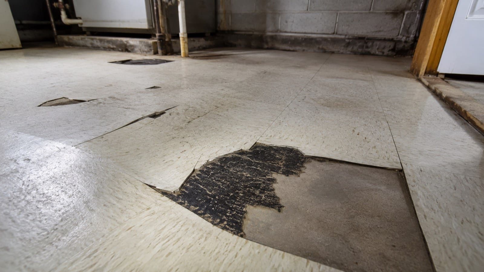 Damaged asbestos floor tile with black mastic adhesive exposed underneath
