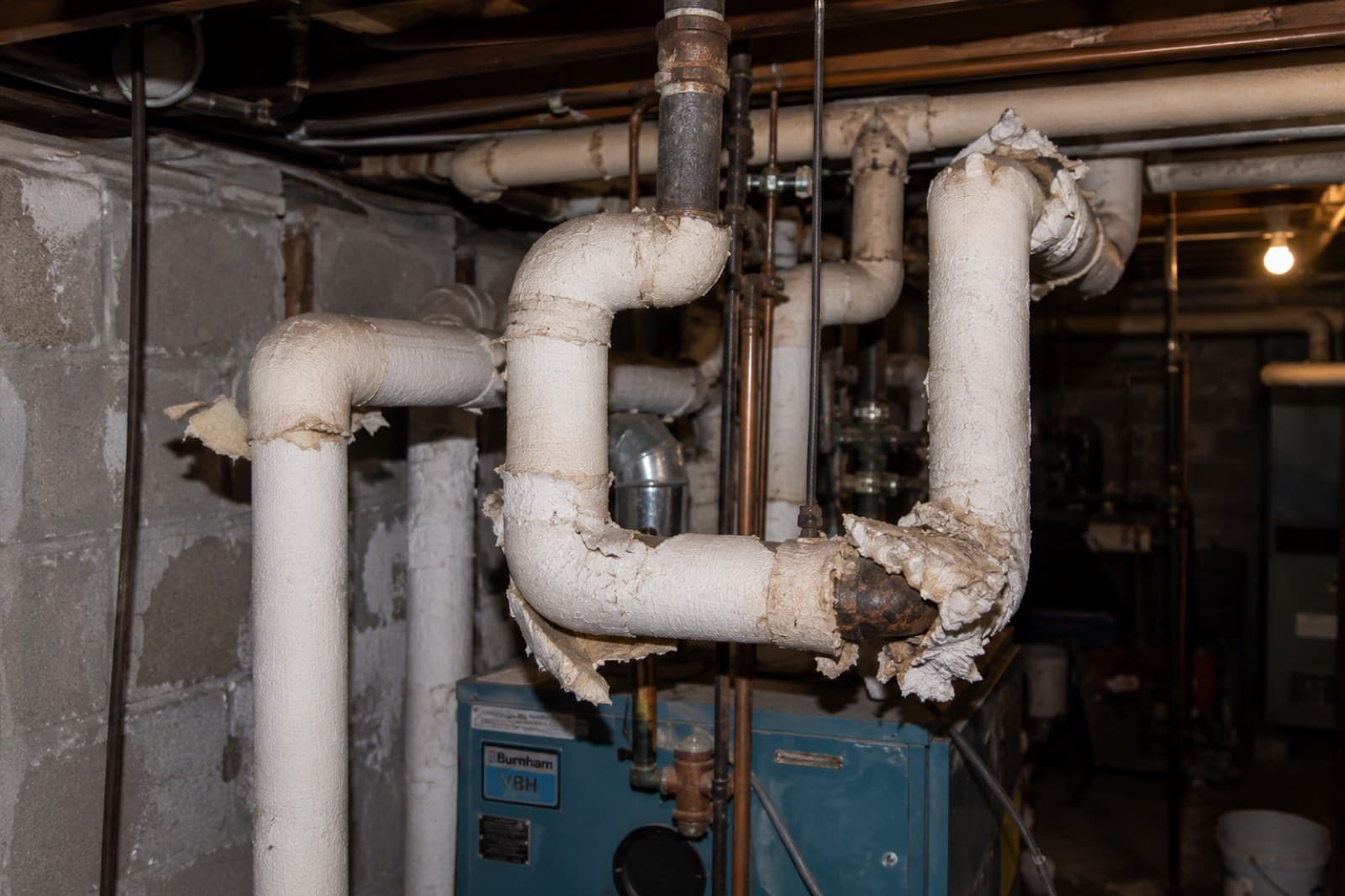 Deteriorating asbestos pipe and boiler insulation lagging in a basement mechanical area