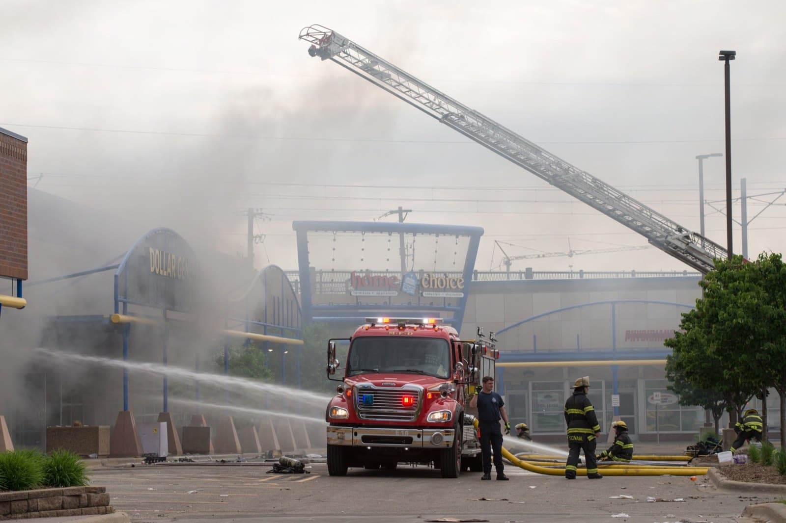 Firefighters with an aerial ladder battling fire and smoke at a multi-tenant commercial building