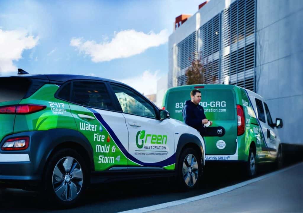 Green Restoration branded fleet vehicles parked outside a commercial building for a cleaning job