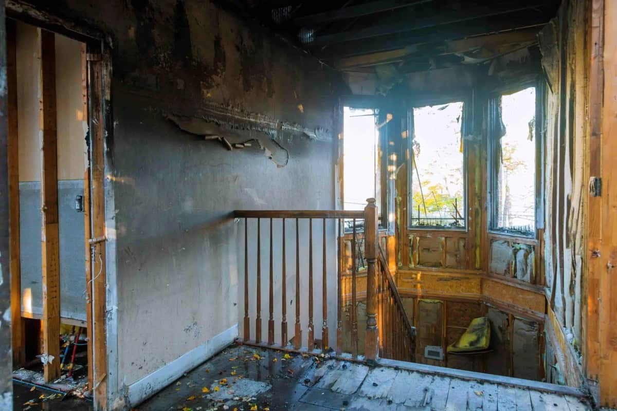 Exterior of a fire-damaged Colonial home with charred roof, smoke-stained siding, and emergency board-up plywood over windows, documented during a Green Restoration IICRC S700 fire damage scope assessment in Deerfield, Franklin County
