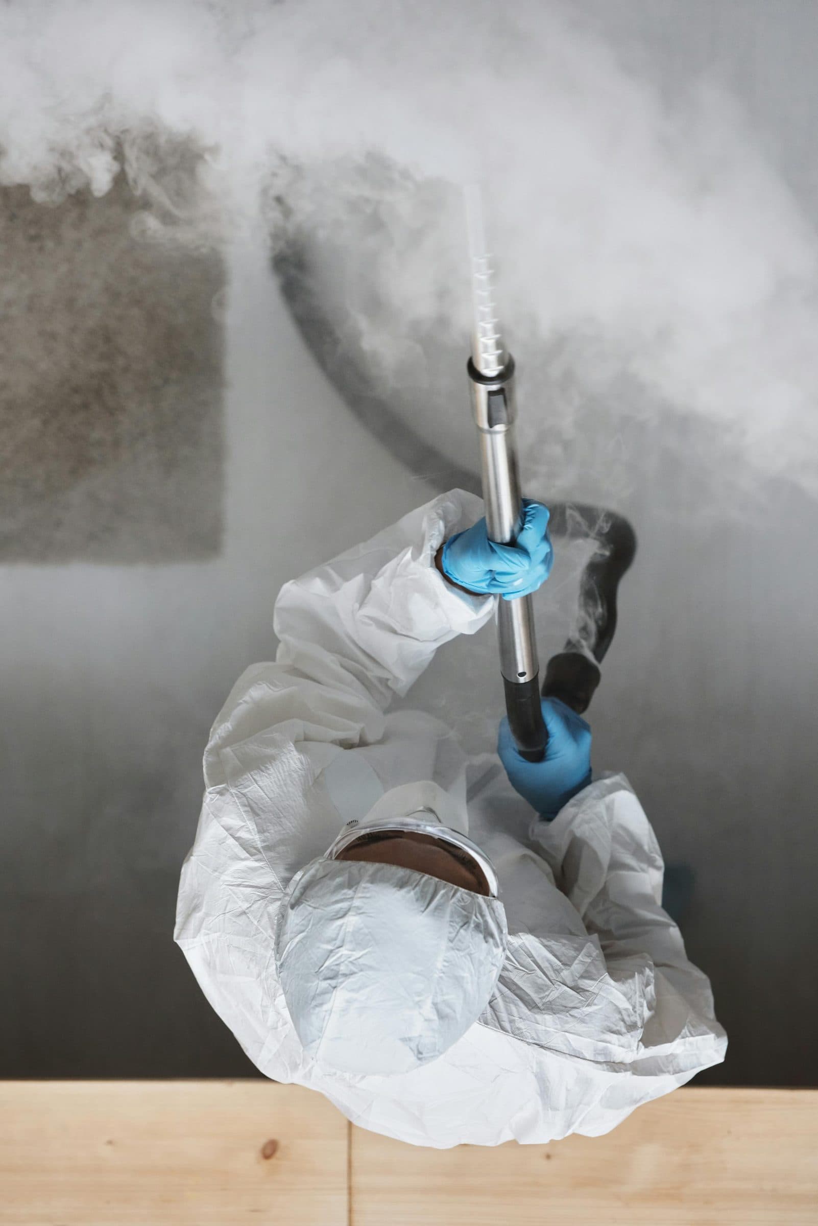 Certified mold inspector holding a calibrated air sampling pump with a spore trap cassette attached, positioned at breathing height in a residential living room while pulling an indoor air sample for AIHA accredited lab analysis