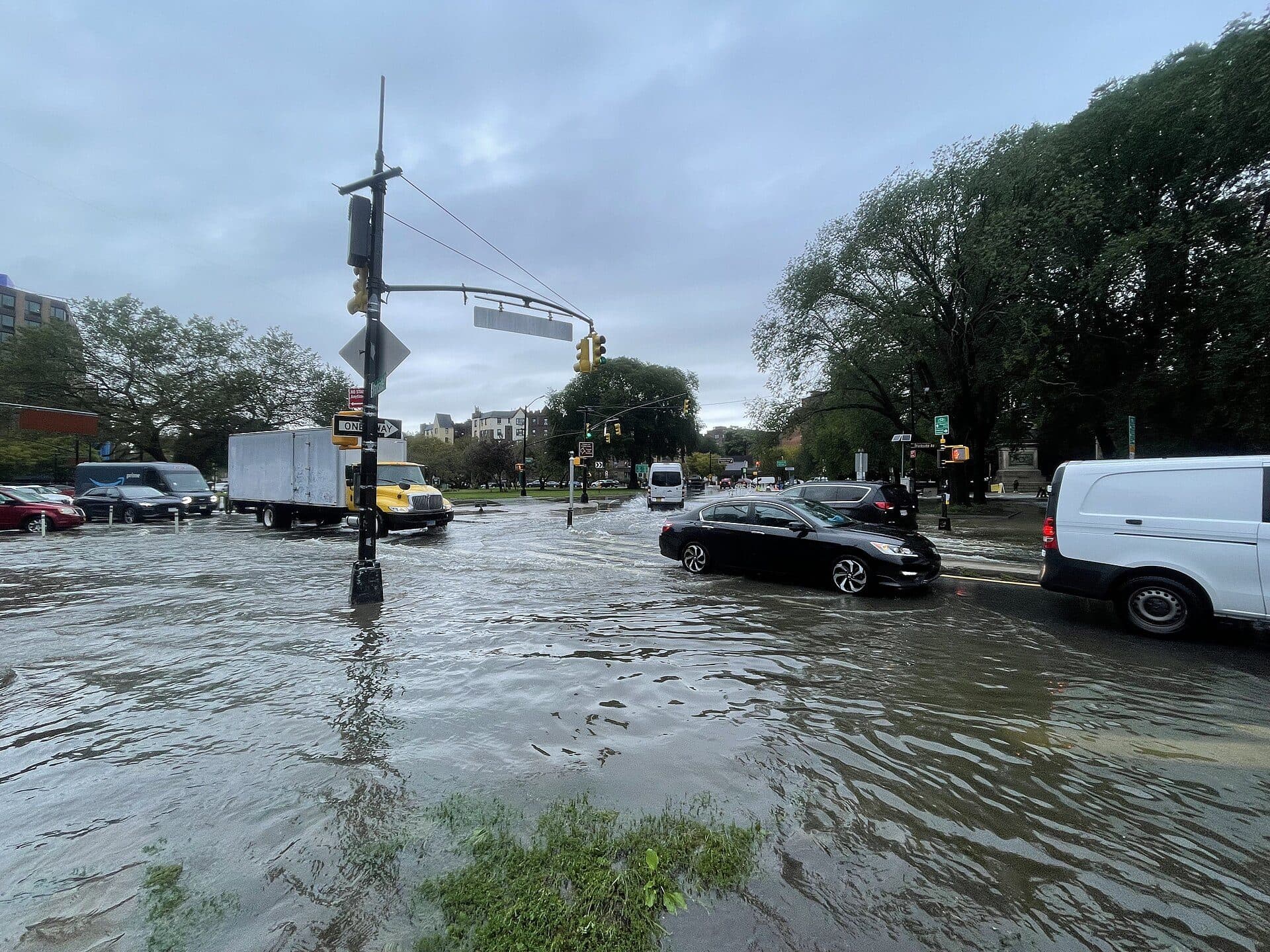 Flooded city intersection during an NYC flash flood with stranded commercial trucks and vans