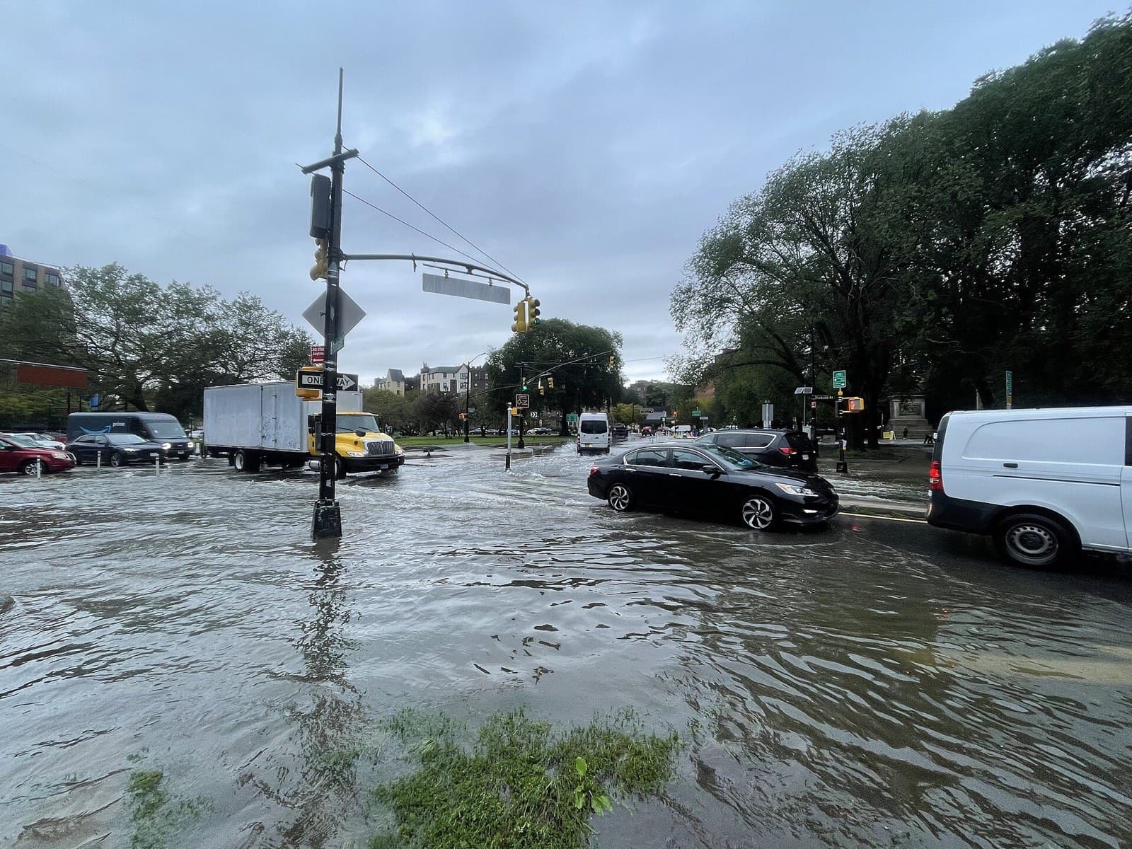 Flooded city intersection during an NYC flash flood with stranded commercial trucks and vans
