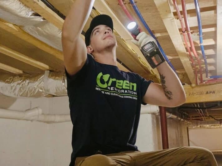 Green Restoration technician inspecting a Deerfield MA crawl space ceiling joist with a flashlight