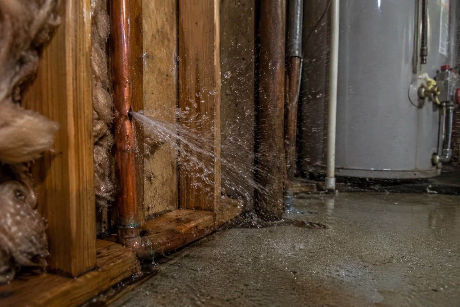 Burst copper supply line spraying water against wall framing and insulation in a basement utility area