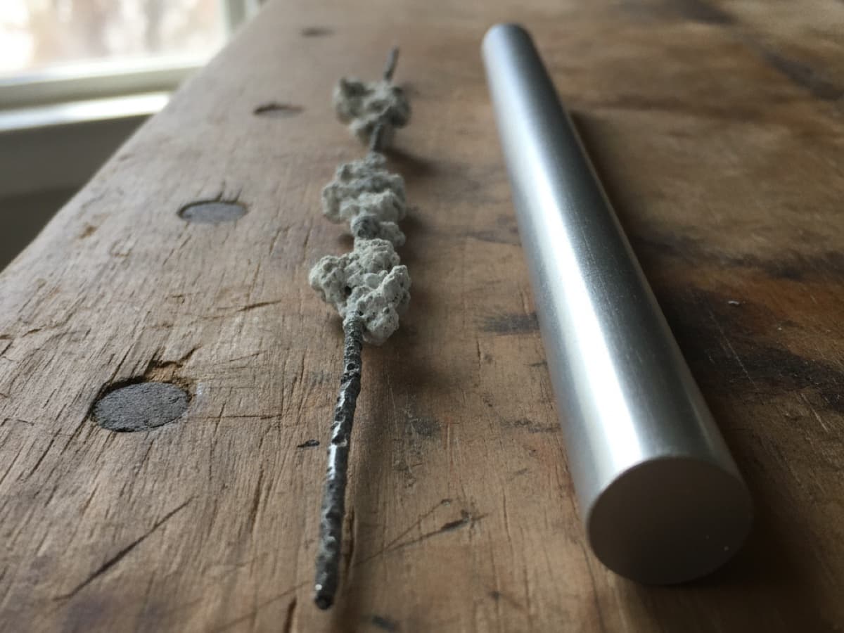 Sacrificial anode rod consumed to a pitted core wire after years in a water heater, beside an unused replacement rod